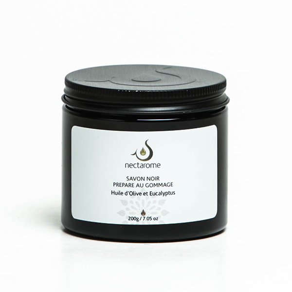 A black jar of Nectarome "Savon Noir Prépare au Gommage" black olive oil soap is shown against a white background. The label highlights olive oil and eucalyptus as key ingredients, with a net weight of 200g (7.05 oz). Perfect for deep cleansing and preparing skin for exfoliation.